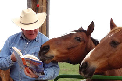 Craig reading a book to two horses at the corral